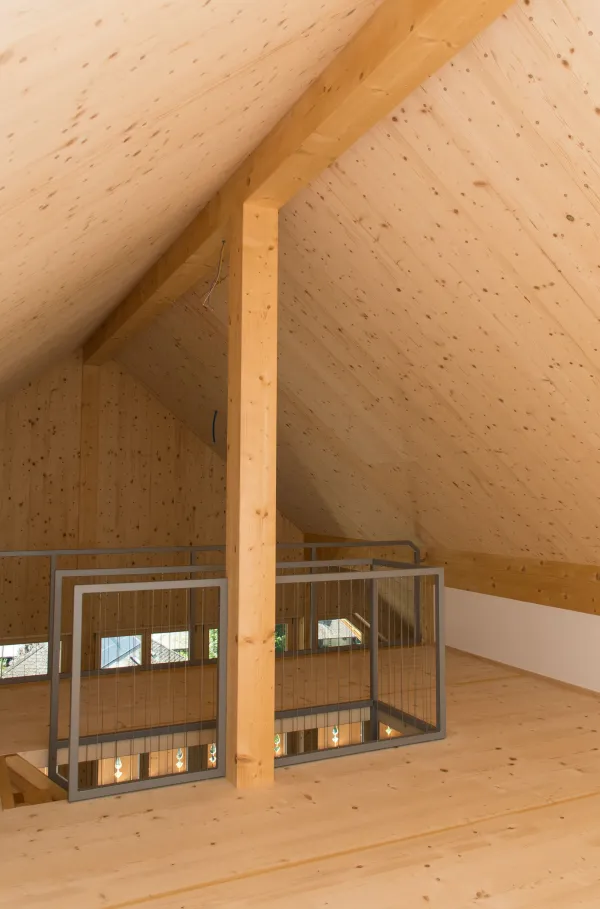 Mehrstöckiges Holzhaus im traditionellen Schweizer Stil mit kunstvoll verzierten Holzbalkonen und grosszügigem Dachüberstand. Die Fassade besteht aus hellem, massivem Holz, umgeben von einer grünen Hanglandschaft bei klarem Himmel.