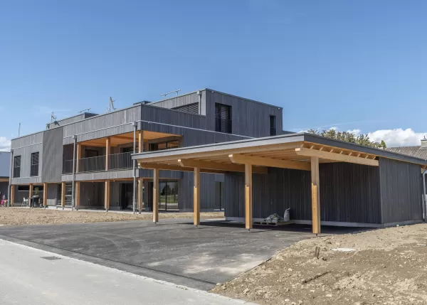 Mehrfamilienhaus Truberholzhaus Recherswil, Schweizer Holz, Truberholzwände sind nicht sichtbar, die Dübel sind nicht sichtbar, Fassade ist vorvergraut, es hat eine Attikawohnung, im Erdgeschoss und Obergeschoss hat es Loggaeinschnitte (Terrasse, Balkon), moderner Neubau, auf dem Dach ist ein Sonnensegel, Flachdach mit Solarpanel, es hat kein Keller dafür ein zusätzliches Gebäude mit Autounterstand und Lagerraum, Umschwung mit Rasen